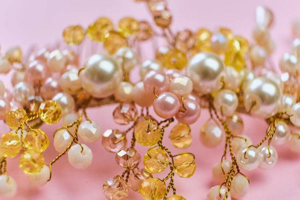 Beautiful hair decoration handmade comb in white and yellow beads, close-up, pink background. Hair ornament made of pearls and beads. Selective focus - Photo, Image