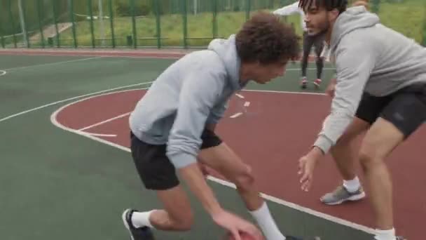 Handheld seuranta laukaus nuori mies dribbling pallo ja yrittää siirtyä puolustaja pelatessaan streetball - Materiaali, video