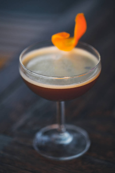 cocktail scuro guarnito con un tocco arancione su un ambiente bar scuro
. - Foto, immagini