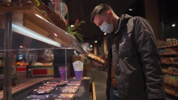Een man met een beschermend medisch masker neemt sushi doos mee uit de supermarkt plank. Nieuwe norm, geen masker geen toegang, sociale afstand en quarantaine covid 19. Japans eten klaar om te eten in lunchbox - Video