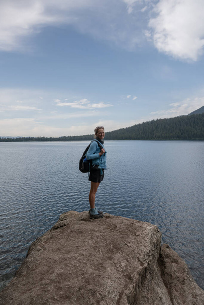 Женщина стоит на краю большого камня вдоль озера Фелпс в национальном парке Гранд-Титон - Фото, изображение