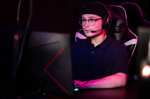 Um jovem ciberatleta usando óculos e um fone de ouvido em um torneio de esports. Retrato de close-up com luz de néon. - Foto, Imagem