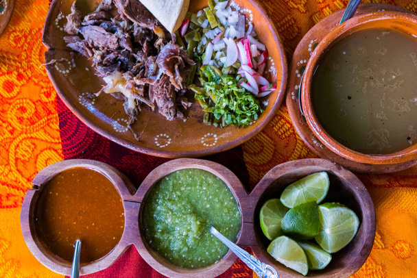 Mexikanisches Lammfleisch, scharfe Saucen und Brühe auf bunter Tischdecke - Foto, Bild