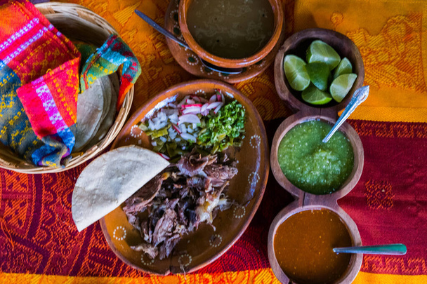 Мексиканское нарезанное мясо ягненка, острые соусы и тортильи на красочной скатерти - Фото, изображение