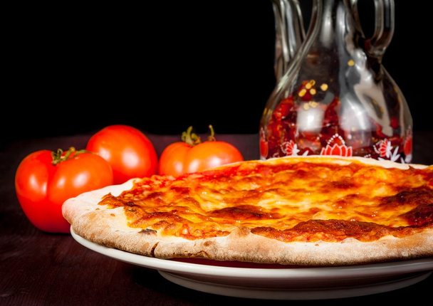 Italiaanse pizza in de buurt van tomaten en pittige olie, typisch Italiaanse pizza - Foto, afbeelding