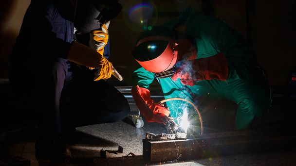Les mécaniciens font des heures supplémentaires à peine la nuit dans une usine. Ingénieurs portant des tenues de sécurité avec combinaisons mécaniques, gants, bottes et casques de soudage travaillant sur le soudage des métaux. - Photo, image