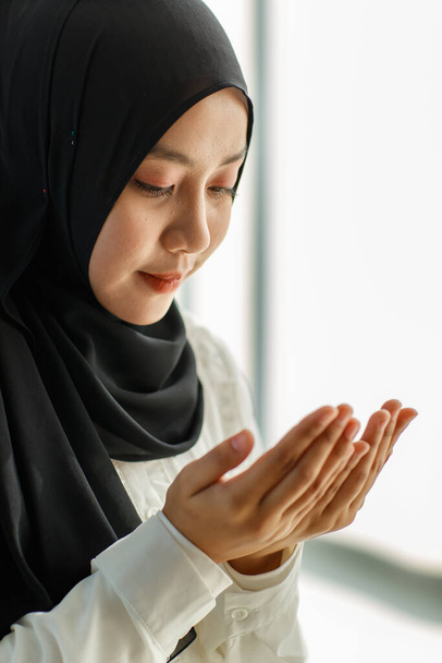 Молодая и красивая азиатская мусульманка в черной вуали сидит на полу и молится с уважением и спокойствием. - Фото, изображение