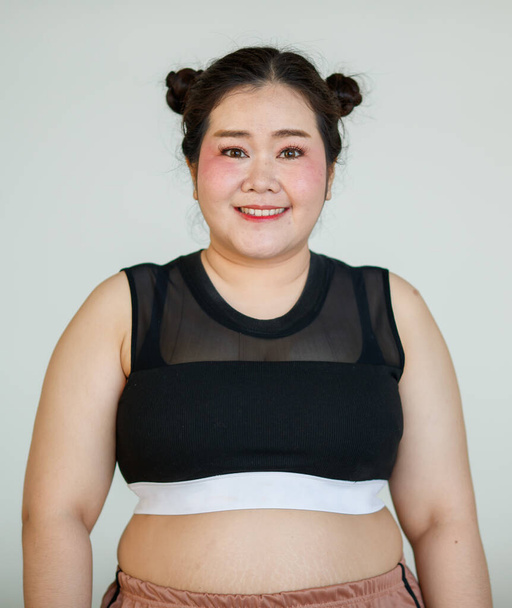 Joven y encantadora linda mujer gorda asiática en ropa deportiva posan a la cámara con un gesto feliz y positivo con confianza en sí mismo y la autoestima. - Foto, imagen