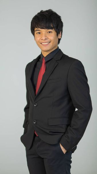 słodkie i przystojny Azji biznesmen wykonawczy wygląd w formalny garnitur stojąc i trzymać rękę w kieszeni i uśmiech do kamery z pewność siebie. - Zdjęcie, obraz
