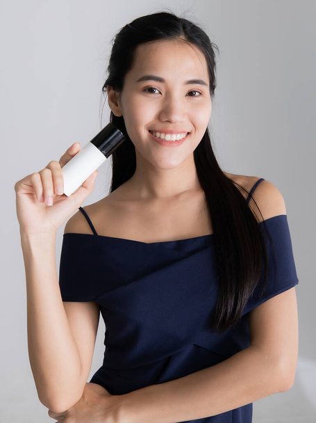Εικόνα του πορτραίτου. Η χαμογελαστή Ασιάτισσα μοντέλο δείχνει κρέμα περιποίησης στο λευκό δωμάτιο του στούντιο. Concept Product camera στούντιο εικόνας - Φωτογραφία, εικόνα