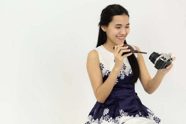 Hymyilevä nuori aasialainen nainen puhdistaa DSLR-kameraa puhaltimella. Studion valkoisessa huoneessa. Concept puhdas kamera valokuvaus ottaa valokuvan - Valokuva, kuva