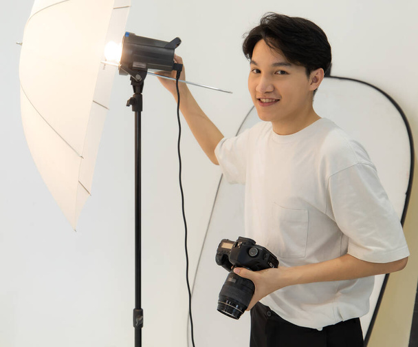 Fotografo asiatico uomo sta prendendo una luce per la fotocamera per scattare foto del modello. Fotografia con fotocamera dslr e flash per scattare foto in camera bianca in studio - Foto, immagini