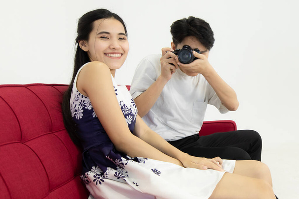 男の写真家と笑顔のガールフレンドを腹立たしいソファの上に座って赤。部屋の雰囲気はスタジオで居心地がいいです。スタジオでのコンセプト居心地の良い写真家. - 写真・画像