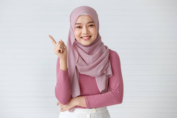 Portrait of a beautiful Muslim woman with a friendly and warm smile posing to the camera with self-confidence. Point finger in a gesture of advertising. - Photo, Image