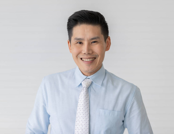 Retrato close up tiro de asiático masculino modelo com curto preto cabelo vestindo luz azul camisa com branco ponto gravata stand sorrindo na frente de branco fundo. - Foto, Imagem