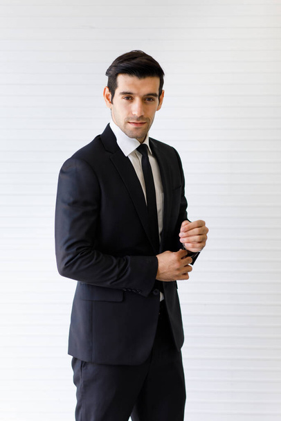 Side view portrait of handsome middle-aged caucasian businessman in a neat formal dark suit with hands in the pocket isolated with white background. He smiles handsomely with a perfect hairstyle - Photo, Image