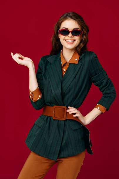 χαρούμενη γυναίκα με κοστούμι γυαλιά ηλίου χαμόγελο περικοπή προβολή κόκκινο φόντο στούντιο - Φωτογραφία, εικόνα