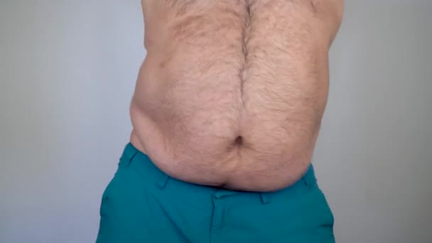 Mann zeigt seinen dicken Bauch und schüttelt seine Falten. Probleme wie schlechte Ernährung und Fettleibigkeit. Der dicke Kerl führt einen Bauchtanz auf. Tag des Abnehmens - Filmmaterial, Video