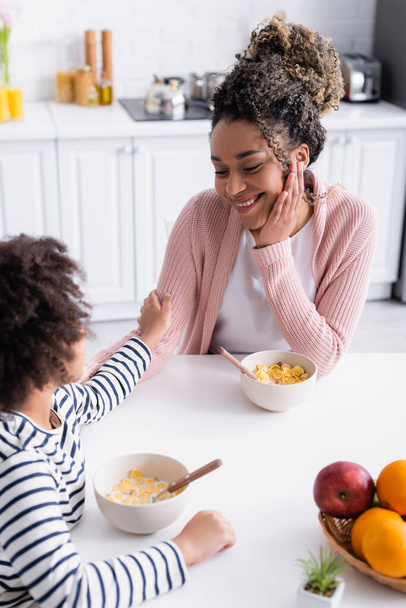 african american kid touching hand of happy mother during breakfast, blurred foreground - Photo, Image