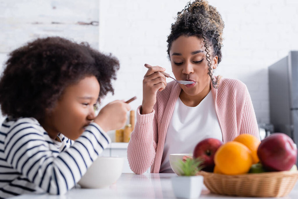 madre e hija afroamericana desayunando cerca de frutas en primer plano borroso - Foto, Imagen