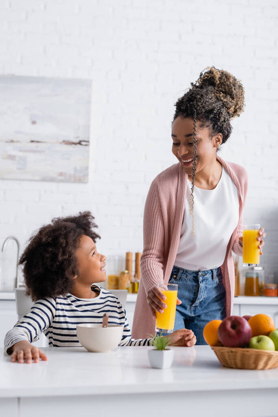アフリカ系アメリカ人の女性がオレンジジュースを飲みながら娘を見ると - 写真・画像