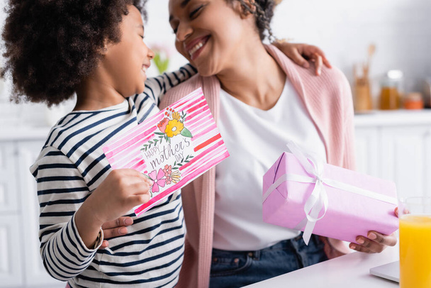 boldog afro-amerikai lány gazdaság boldog anya nap kártya közelében elégedett anya elmosódott háttér - Fotó, kép