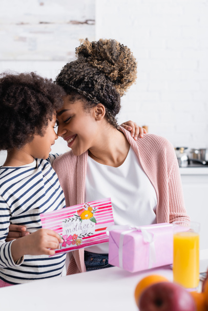 Mutlu Afro-Amerikan kadını kızını kucaklıyor ve ön planda mutlu anneler günü kartını tutuyor. - Fotoğraf, Görsel
