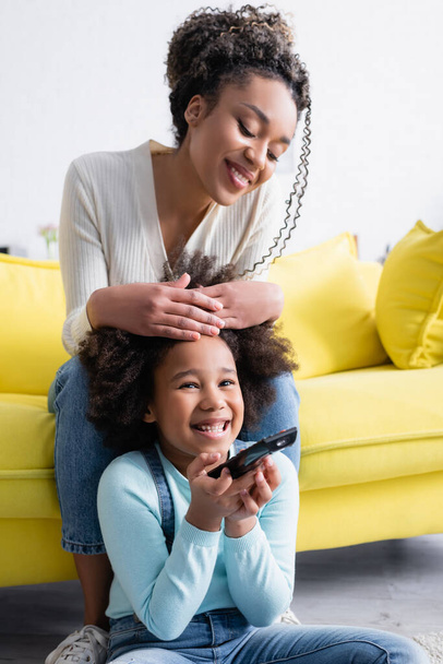 opgewonden Afrikaans amerikaans kind met afstandsbediening terwijl het kijken naar tv in de buurt gelukkig moeder - Foto, afbeelding