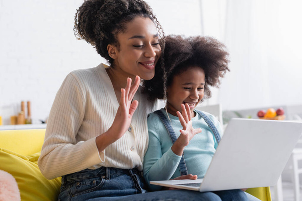 幸せなアフリカ系アメリカ人の母親と娘がノートパソコンでビデオ通話中に手を振って - 写真・画像