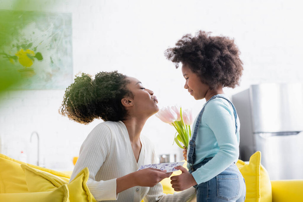 donna afroamericana con felice carte madri giorno soffiando aria bacio alla figlia con tulipani freschi - Foto, immagini
