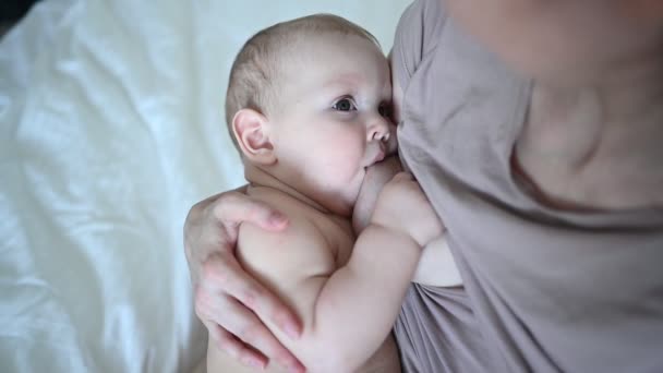 Fiatal anya újszülött aranyos csecsemő meztelen kisfiú az ágyon, tartja őt a karját, ölelés és szoptat anyatejjel. Egészséges gyermek, a kórház és a boldog anyaság fogalma. Gyermekszoba - Felvétel, videó
