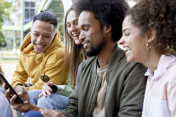 Szczęśliwa grupa młodych przyjaciół korzystających z telefonu komórkowego                                - Zdjęcie, obraz