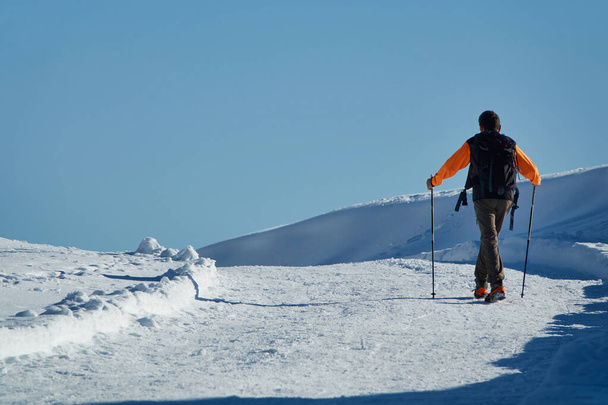 İskandinav yürüyüşleri için sopayla karda yürüyen adam ve kramponlu botlar - Fotoğraf, Görsel