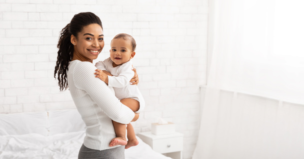 Молодая чернокожая мама держит малыша Тоддлера, позирующего в помещении, Панорама - Фото, изображение