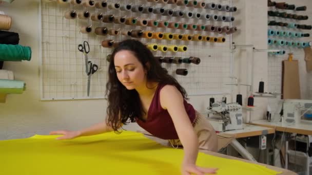 sastre femenino endereza la tela amarilla para el trabajo en la mesa en el estudio. Concepto de proceso de trabajo creativo. Concepto de diseñador de moda para pequeñas empresas - Metraje, vídeo