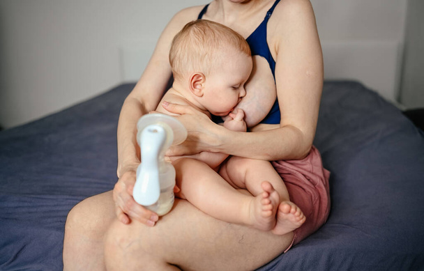 Madre joven con bebé recién nacido lindo bebé desnudo, sosteniéndolo en los brazos, usando un extractor de leche abrazando y amamantando con leche materna. Niño sano, concepto de hospital y maternidad feliz. Vivero. - Foto, Imagen