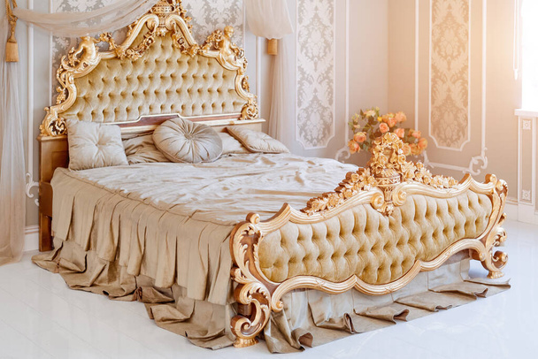 Camera da letto di lusso in colori chiari con dettagli di mobili dorati. Grande confortevole letto matrimoniale reale in elegante interno classico. - Foto, immagini