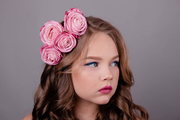 брюнетка дівчина-підліток з рожевими трояндами у волоссі на сірому фоні. фотографія моди. квіти в завитках на голові
. - Фото, зображення