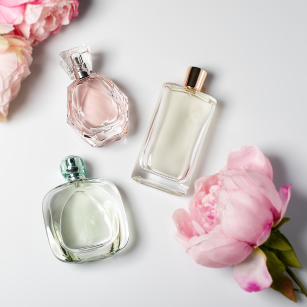 Arka planda çiçekler olan parfüm şişeleri. Parfüm, kozmetik, parfüm koleksiyonu. Düz yatıyordu. - Fotoğraf, Görsel
