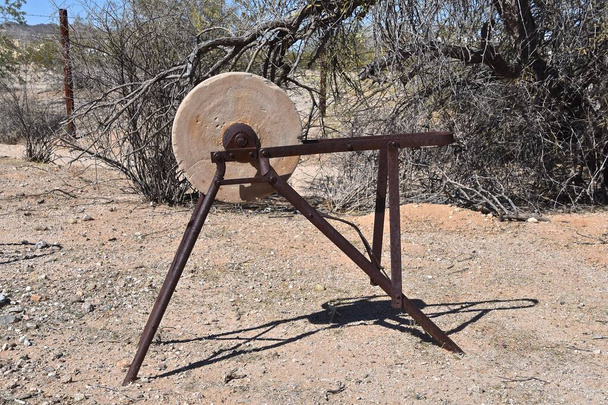 A very old grinding wheel with a rusty frame is left outside in a desert setting.  - Photo, Image