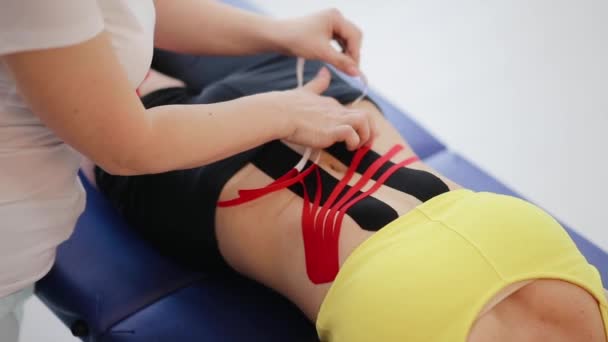 Fisioterapeuta haciendo terapia de cinta kinesio alternativa en el abdomen de la mujer - Imágenes, Vídeo