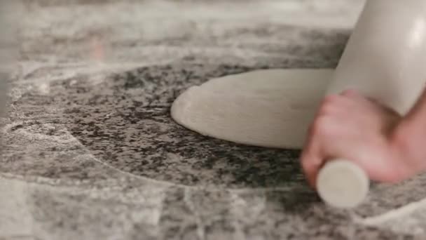 Close up male hands rolls out dough using rolling pin cooking pizzeria. Baker rolling pizza dough on table before baking. Male hands rolling dough on wooden table - Footage, Video