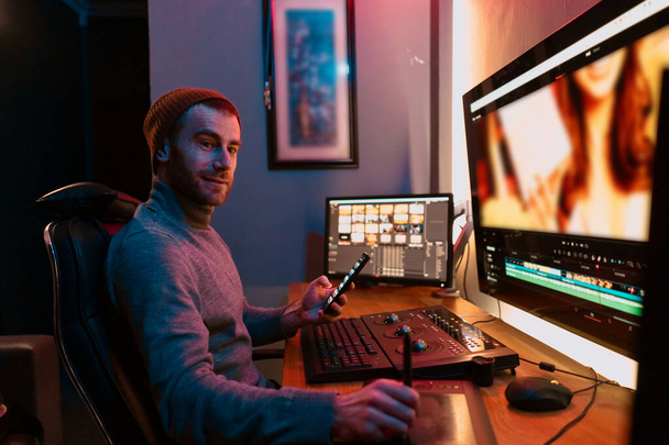 Masculino Video Editor sentado em seu computador usando telefone - Foto, Imagem