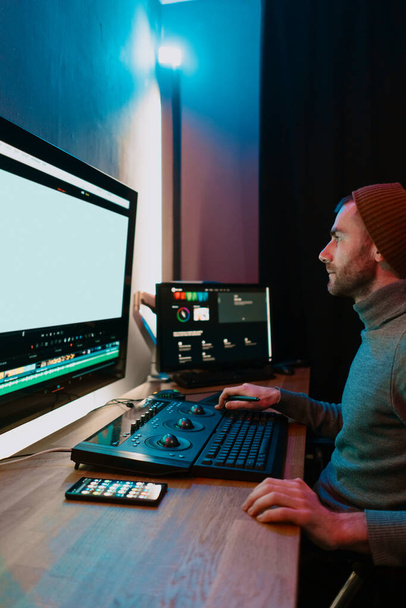 Αρσενικός επεξεργαστής βίντεο που εργάζεται στον προσωπικό υπολογιστή του με μεγάλη κενή οθόνη - Φωτογραφία, εικόνα