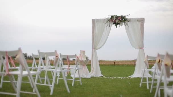 Ceremonia ślubna. Bardzo piękny i stylowy łuk weselny, ozdobiony różnymi świeżymi kwiatami i białą szmatką, stojący na zielonej trawie - Materiał filmowy, wideo