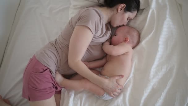 Молодая мать лежит с новорожденным милым голым младенцем на кровати, держит его на руках, обнимает и кормит грудным молоком. Здоровый ребенок, концепция больницы и счастливое материнство. Детская комната - Кадры, видео