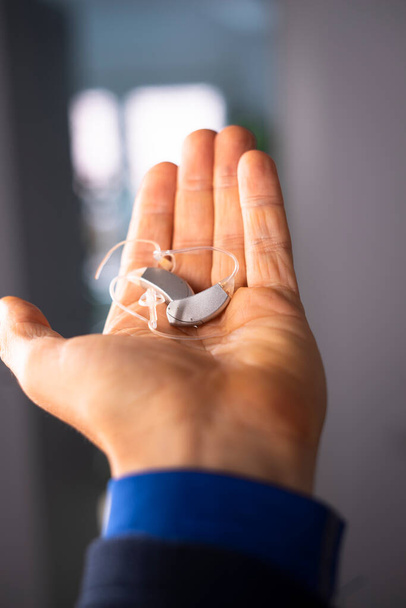 Σύγχρονο ψηφιακό ακουστικό βοήθημα στο αυτί μεσήλικας 40άρης άντρας στο χέρι - Φωτογραφία, εικόνα