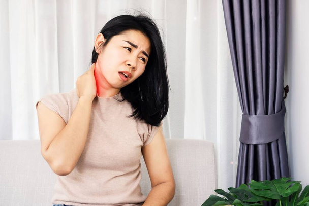 źle Azji kobieta cierpi na ból szyi siedzi na kanapie ręka masaż jej ból szyi - Zdjęcie, obraz