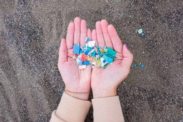 Mujer sosteniendo una mano llena de coloridos fragmentos de plástico, basura recogida en la playa, contaminando el océano y poniendo en peligro la vida silvestre, el esfuerzo ambiental y el deber de reciclar y reducir los residuos - Foto, Imagen