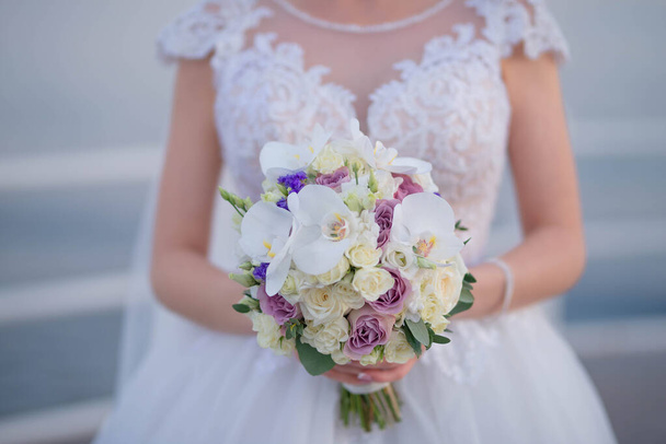 Hermosa novia caucásica con un elegante vestido blanco mientras sostiene un ramo grande con orquídeas blancas y rosas de color pastel, hermoso arreglo de flores como un accesorio para el día de la boda - Foto, imagen